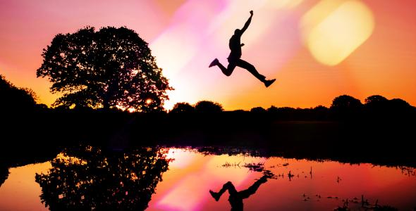 A silhouette of a man jumping over a body of water