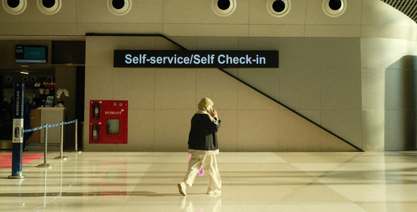 A person walks through an empty airport in front of a sign stating 'self service/self check-in'