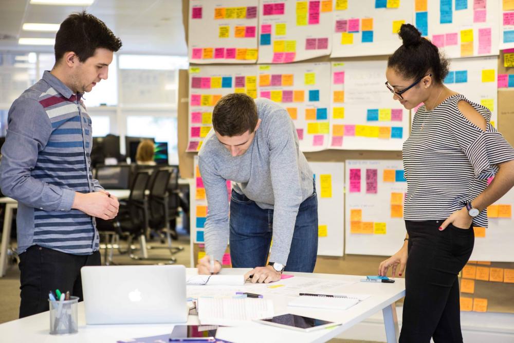 Meeting mit drei Mitarbeitern vor einer Post-it Wand