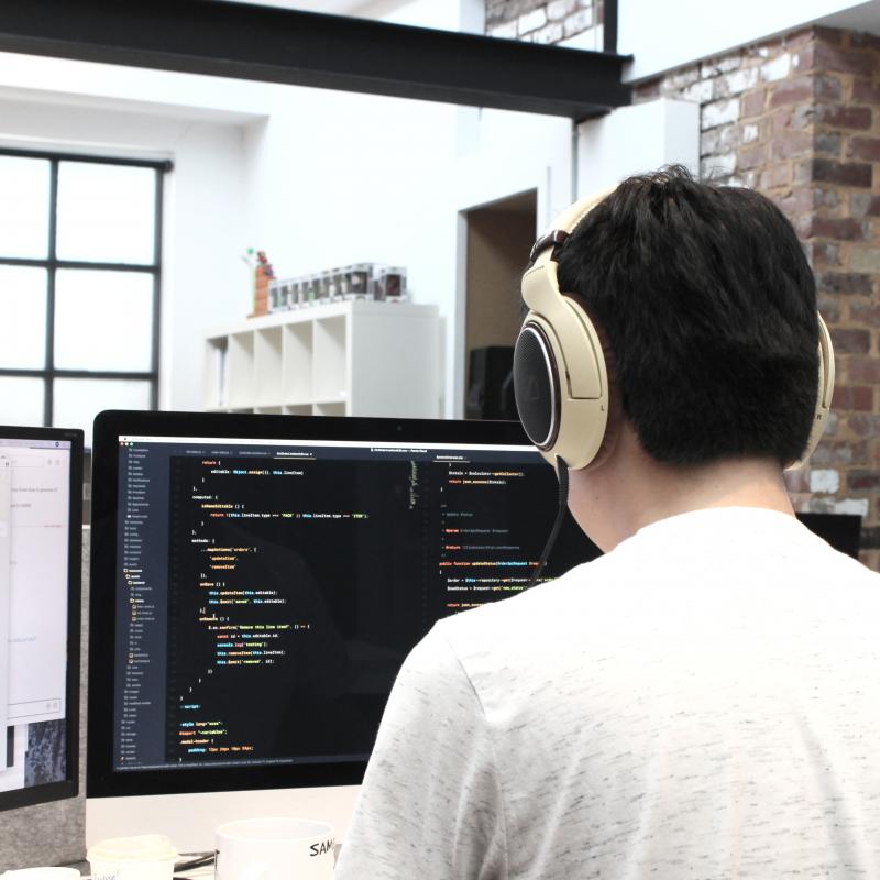Mann programmiert Code und sitzt mit Kopfhörer vor einem Computer