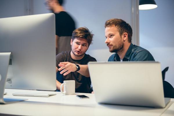 two men consulting over a laptop and screen